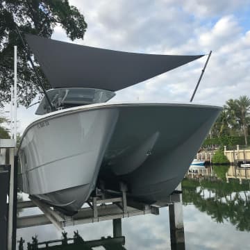 Charcoal shade sail rigged over a white center console boat on a canal lift